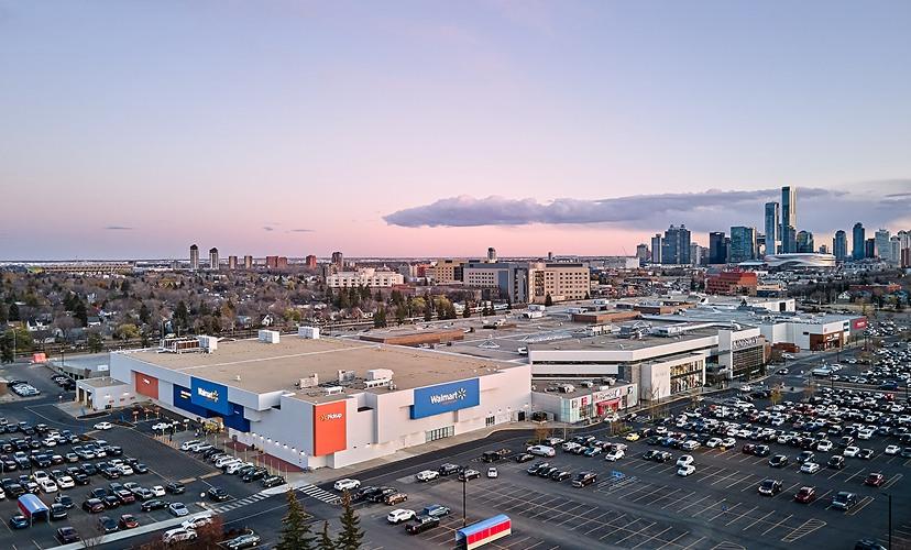 Aerial view of a Walmart-anchored mall at dusk with the Calgary skyline behind