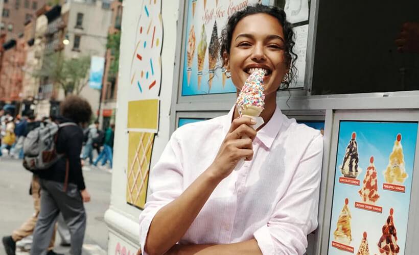 Smiling woman eating a sprinkle-topped soft ice cream cone on a city street