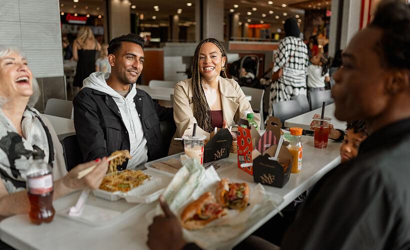 Friends laughing over takeout meals together in the mall food court